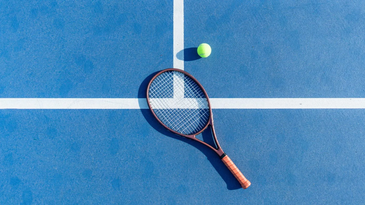 High-angle view of tennis racket and ball on blue court surface