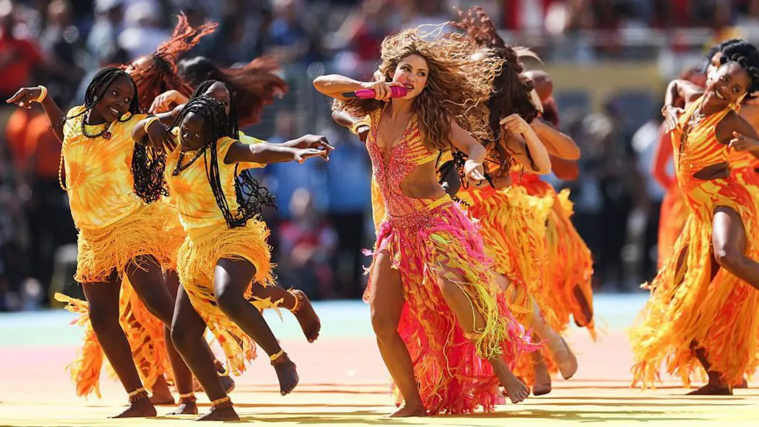 Getty Images Shakira dancing in a pink, yellow, orange and red flowing outfit with back-up dancers